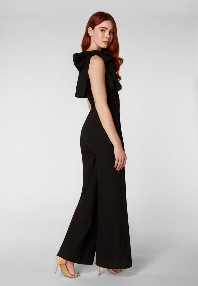 Czarny kombinezon z szerokimi nogawkami i falbanistym dekoltem. Wykonany z gładkiego materiału, ma dopasowaną górę i luźne nogawki.