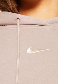 Felpa leggera color malva con tessuto testurizzato, dotata di cappuccio con cordino e logo Nike swoosh crema sul petto.