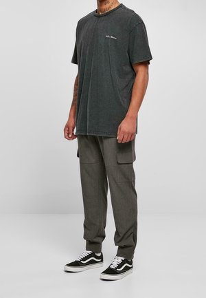 Dunkelgraues Herren-T-Shirt aus Baumwolle mit rundem Ausschnitt, kombiniert mit hellgrauer Cargo-Hose mit Seitentaschen und schwarz-weißen Sneakers.