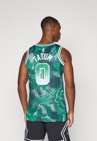 Groen basketbalt-shirt met een gestructureerd grafisch patroon, witte afwerking, nummer "0" en de naam "TATUM" op de achterkant. Draagt met zwarte shorts.