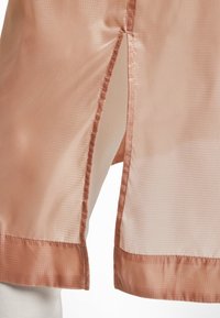 Persikofärgad genomskinlig tyg med ett mönster av texturerad rutnät, med en delad detalj och satinbård längs kanten för kontrast.