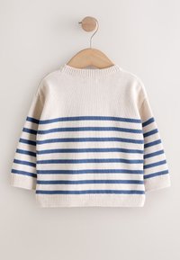Pull en maille blanc avec des rayures horizontales bleues, manches longues et poignets côtelés, accroché à un cintre en bois sur un fond clair.