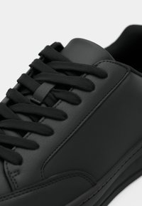 Μαύρο δερμάτινο αθλητικό παπούτσι με επίπεδα μαύρα κορδόνια, λεία υφή και αντίθετη ραφή. Στρογγυλερή μύτη και επενδεδυμένος γιακάς για άνεση.