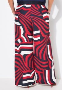 Wide-leg trousers in a vibrant red, navy, and white abstract pattern; made from lightweight fabric, featuring a comfortable elastic waistband and pockets.