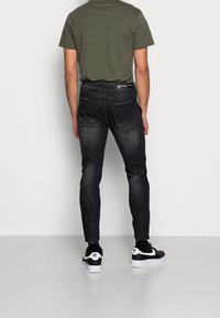 Vaqueros pitillo negros con lavado desvaído, detalles cosidos y dos bolsillos traseros. Combinados con una camiseta de manga corta verde oliva y zapatillas negras.