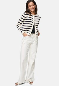 Cardigan rayé en crème et marine, avec un col rond, une fermeture à boutons et des manches longues, associé à un pantalon blanc à jambes larges et des sandales.
