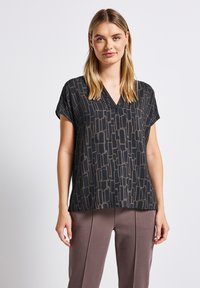 Blusa nera a scollo a V con maniche corte, caratterizzata da un motivo geometrico nei toni di grigio. Tessuto morbido, vestibilità rilassata e texture delicata.