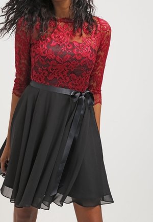 Bodice en dentelle rouge avec manches trois-quarts, jupe en chiffon noir, taille cintrée avec un ruban en satin, silhouette évasée.
