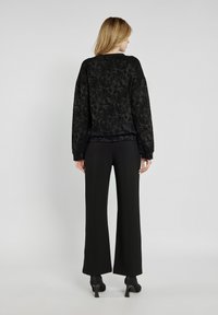 Czarny sweter w wzór z długimi rękawami, okrągłym dekoltem i wzorem w paisley, w połączeniu z czarnymi spodniami z wysokim stanem i szpilkami.
