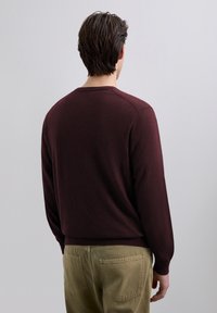 Bordeauxrode trui met een ronde hals, geribbelde manchetten en zoom, gecombineerd met olijfgroene broek. Zachte textuur en eenvoudig ontwerp.