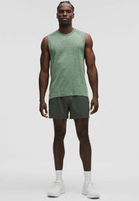 Grön ärmlös topp med ett strukturerat mönster, kombinerad med mörkgröna shorts. Modell i vita sportskor och strumpor.
