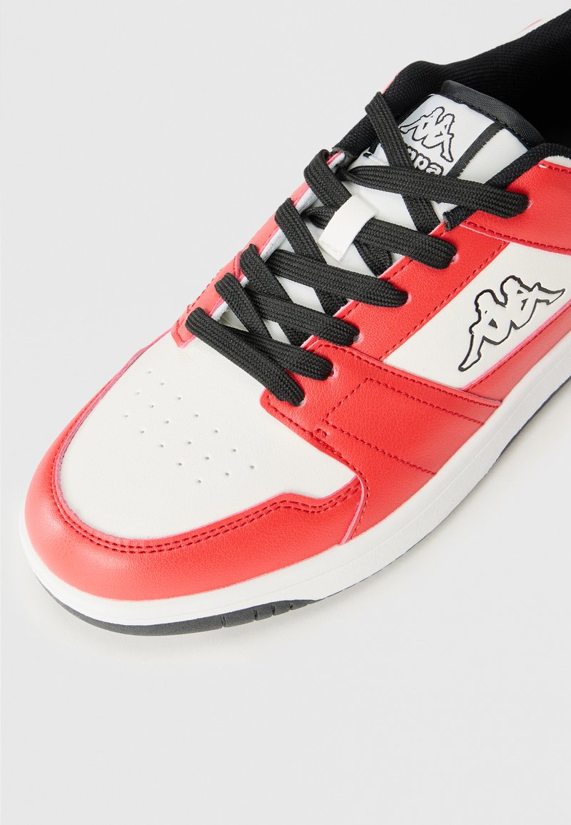 Zapatilla roja y blanca con acabado de cuero suave, cordones negros, puntera perforada y detalle del logo en el lado.