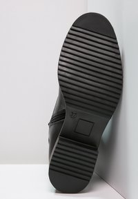 Botte en cuir noir avec une semelle en caoutchouc nervurée. Comprend une fermeture éclair intérieure et une étiquette indiquant la taille 37. Texture lisse avec un design élégant.