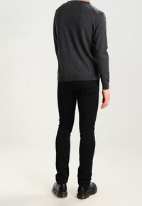 Szary sweter z długimi rękawami, ściągaczami na rękawach i okrągłym dekoltem; zestawiony z czarnymi, dopasowanymi spodniami oraz czarnymi butami, widziany od tyłu.