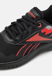 Baskets noires pour le sport avec tige en mesh, accents rouges et semelle texturée. Présente le logo Reebok, des lacets et un design latéral distinctif.