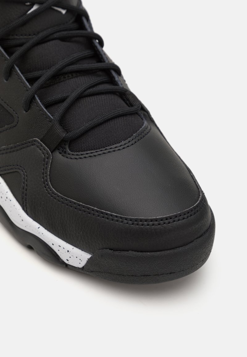 Chaussure de sport noire avec une tige en cuir lisse, une languette en maille texturée et des accents de semelle blanche mouchetée. Présente un système de laçage traditionnel.