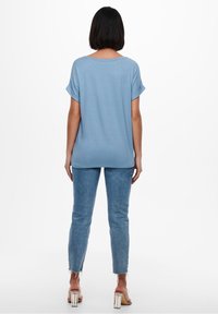 Light blue, short-sleeved t-shirt with a relaxed fit. Paired with fitted, slightly frayed jeans and clear block-heeled sandals.