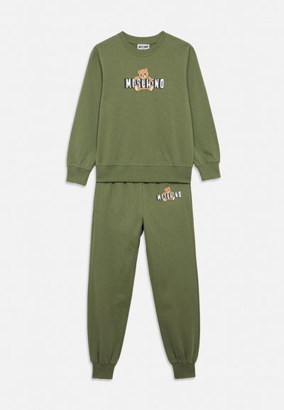 Ensemble sweat-shirt et joggers vert olive avec poignets côtelés, présentant un ours en peluche et le logo "Moschino" sur le haut et le pantalon.