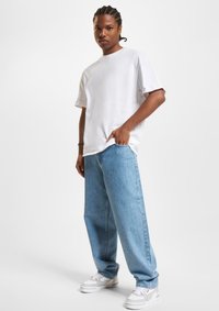 White cotton crew-neck t-shirt paired with light blue denim jeans, featuring a relaxed fit and side pockets, complemented by gray sneakers.