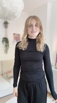 Sort langærmet top med høj hals, lavet af et glat, strækbart stof; kombineret med sorte sweatpants med snøre. Lys baggrundsdekoration.