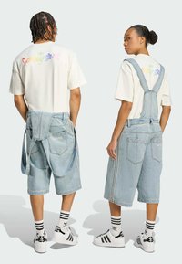 Denimové šortky v svetlomodrej farbe s nastaviteľnými popruhmi, voľné šortky a logo na chrbte. Štýlované s bielymi tričkami a čierno-bielymi teniskami.