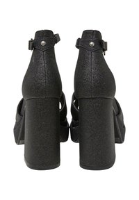 Pair of black glittery high-heeled sandals with ankle straps and chunky block heels shown from the back on a white background.