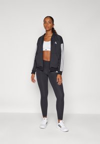 Black athletic jacket with white stripes, paired with a white sports bra and black leggings. White shoes, smooth texture, zipper pockets.