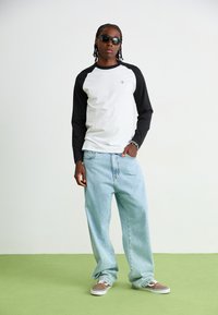 Sorte og hvide langærmede skjorte med rund halsudskæring, parret med lyseblå løstsiddende jeans og brune sneakers med hvide detaljer.