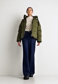Giacca imbottita verde oliva con cappuccio, maglietta bianca con motivo, jeans a vita alta blu scuro e scarpe chunky nere. Design semplice, vestibilità casual.