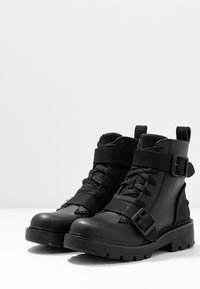Czarne skórzane botki o wojskowym stylu, z fakturowaną powierzchnią, wyposażone w sznurowadła, paski z klamrami i wytrzymałą podeszwę.