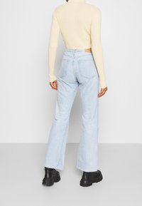 Jeans acampanados de un azul claro con un lavado ligeramente desvanecido, bolsillos traseros y una cintura alta. Combinados con una blusa ajustada de color crema y corte cropped.