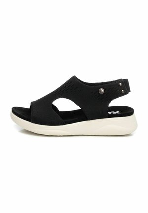 Sandalia negra con parte superior de malla transpirable, punta abierta y diseño recortado; cuenta con una suela de goma blanca y correa ajustable con acentos metálicos.