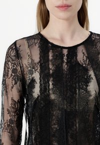 Black lace top featuring floral patterns, sheer texture, long sleeves, and a round neckline, creating a delicate, layered appearance.