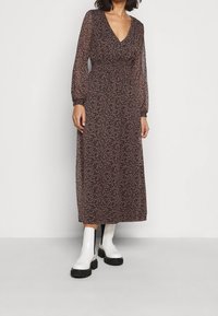 Langes, durchscheinendes Kleid mit V-Ausschnitt, braunem Grundton und kleinen floralen Mustern in Pink und Weiß. Mit langen Ärmeln und taillierter Passform.