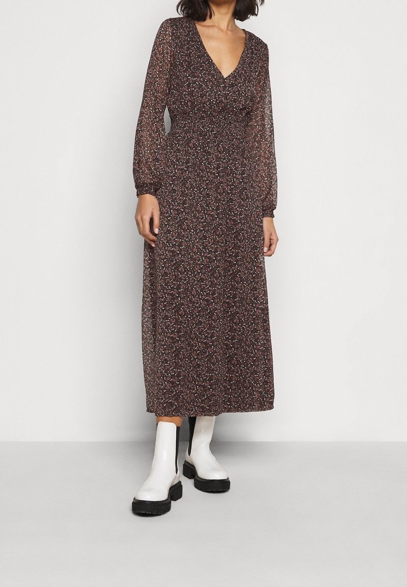 Langes, durchscheinendes Kleid mit V-Ausschnitt, braunem Grundton und kleinen floralen Mustern in Pink und Weiß. Mit langen Ärmeln und taillierter Passform.