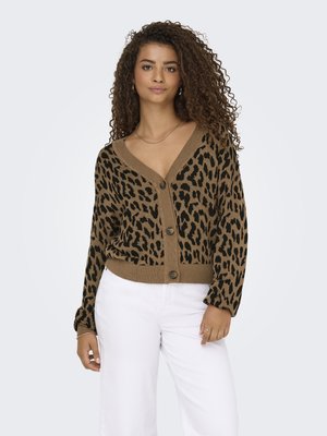 Cardigan imprimé léopard en marron et noir, avec un col en V, fermeture par boutons, et des poignets et un ourlet côtelés. Assorti à un pantalon blanc.