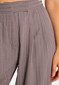 Pantalon gris en tissu texturé avec des rayures verticales en sequins, une taille plate et une coupe élégante et ample.