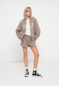 Tan hooded sweatshirt with logo, paired with matching shorts. Ensemble features a casual fit, soft fabric, and black high-top sneakers.