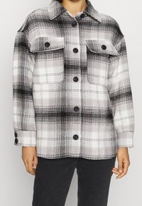 Czarna i biała kurtka koszulowa w kratę z kołnierzykiem, dwoma przednimi kieszeniami i zapięciem na guziki. Wykonana z miękkiego materiału o teksturowanej powierzchni.