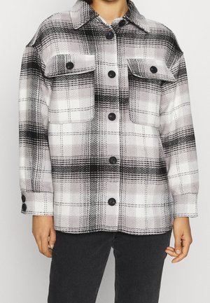 Veste chemise à carreaux noir et blanc avec col, deux poches avant et fermetures à boutons. Fabriquée en tissu texturé doux.