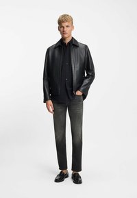 Czarna skórzana kurtka z kołnierzem, noszona na czarnej koszuli. W zestawie szare dżinsy i czarne mokasyny. Jednolite tło.