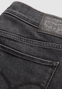 Svarta denimjeans med en strukturerad yta, som har en stickad midja och en rektangulär läderlapp med präglade grafiska mönster.