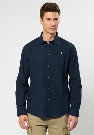 Camicia a maniche lunghe blu navy in tessuto texturizzato, con chiusura a bottoni davanti e un piccolo emblema sul petto.