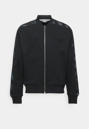 Black zip-up sweatshirt made of soft fabric, featuring a ribbed collar and cuffs, and patterned accents along the sleeves. Embossed logo on front.
