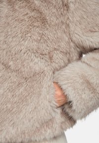 Faux-Fur-Jacke in hellem Beige mit weicher, flauschiger Textur und lässigem Schnitt. Verfügt über Seitentaschen und breite, plüschige Bündchen.