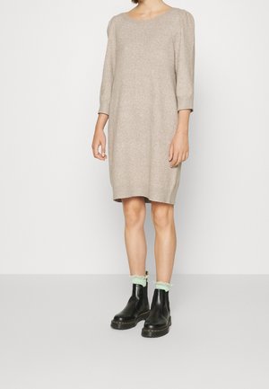 Robe en tricot beige à manches trois quarts, décolleté rond et coupe décontractée. Assortie à des bottines noires et des chaussettes vert menthe avec bord en dentelle.