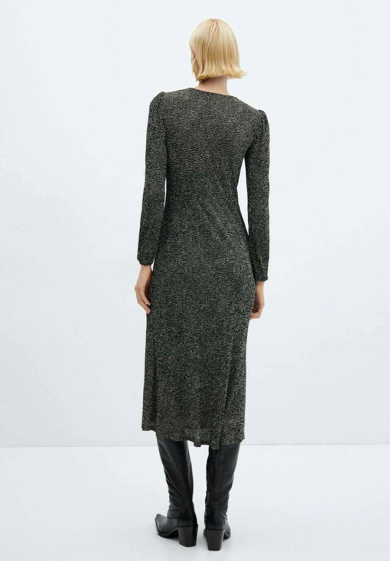 Abito a maniche lunghe a righe bianche e nere con una silhouette aderente, lunghezza al ginocchio e uno spacco sul retro, abbinato a stivali neri al ginocchio.