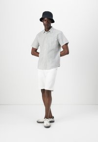 Stripet kortærmet skjorte i lysegrå og hvid, parret med hvide shorts og grå sneakers med sorte akcenter. Sort bucket hat.