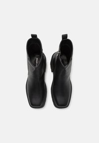 Botas de cuero negro hasta el tobillo con textura suave, punta cuadrada, cremalleras laterales y lengüetas de tiro. Suelas de goma planas para tracción y comodidad.
