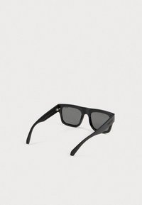 Fekete, téglalap alakú Polaroid napszemüveg sötét lencsékkel, nyitva fekszik egy fehér felületen, a márkanevével a szárán.